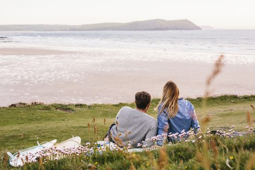 A couple watches as the sun sets over Polzeath Beach, North Cornwall