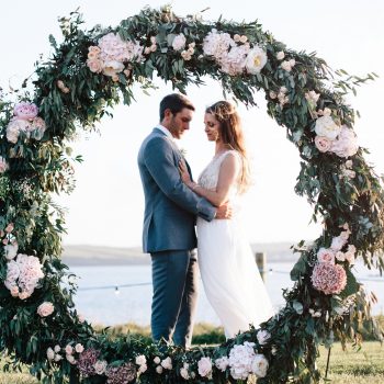 A bride and groom and a floral moongate at Porthilly, Rock